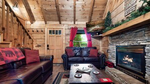 A cozy log cabin interior with a fireplace, leather sofas, and a stone fireplace surround. - Rustic Escape: Nature Views, Hot Tub & Fire Pit (Sevierville)