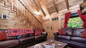 A wooden interior with two leather sofas, a coffee table, and a door with a 'GUEST' sign. - Rustic Escape: Nature Views, Hot Tub & Fire Pit (Sevierville)