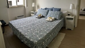 A neatly made bed with a patterned bedspread, two bedside tables with lamps, a radiator, and a window with blinds. - House facing the sea (Passoscuro)