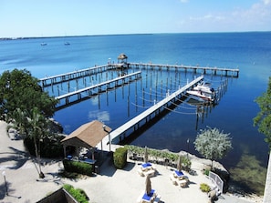A pier extending into calm blue waters with a small hut and lounge chairs on the beach.