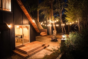 Une maison moderne avec une entrée dotée d’une porte en verre, une terrasse en bois et des guirlandes lumineuses.