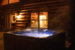 Ein Whirlpool vor einer Blockhütte mit einer Holzterrasse und einem Stuhl.