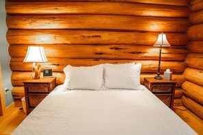 Una habitación de cabaña de madera con una cama, dos mesitas de noche, una lámpara y un radio.