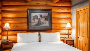 Un dormitori d'estil cabana de fusta amb un llit, dues làmpades de nit, un quadre amb marc a la paret i una porta de fusta.