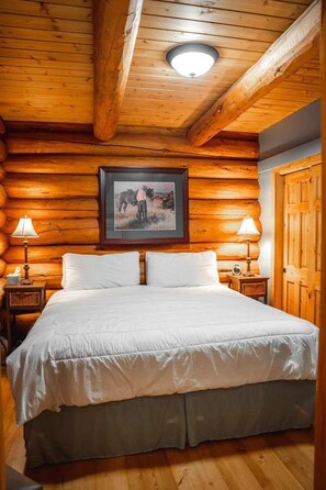 Ein schlafzimmer im Chalet-Stil mit einem Bett, zwei Nachttischlampen, einem gerahmten Bild an der Wand und einer Holztür.
