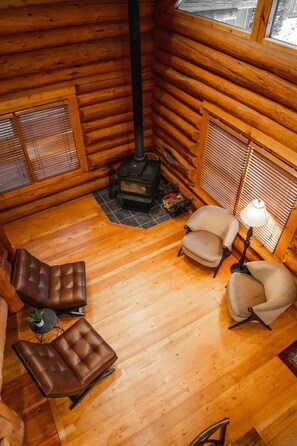 L’intérieur d’une cabane en rondins, avec une cheminée, deux fauteuils en cuir, une lampe et une petite table.