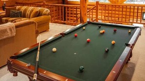 Ein Holzinterieur mit Billardtisch, einer Couch und Blick durch große Fenster.