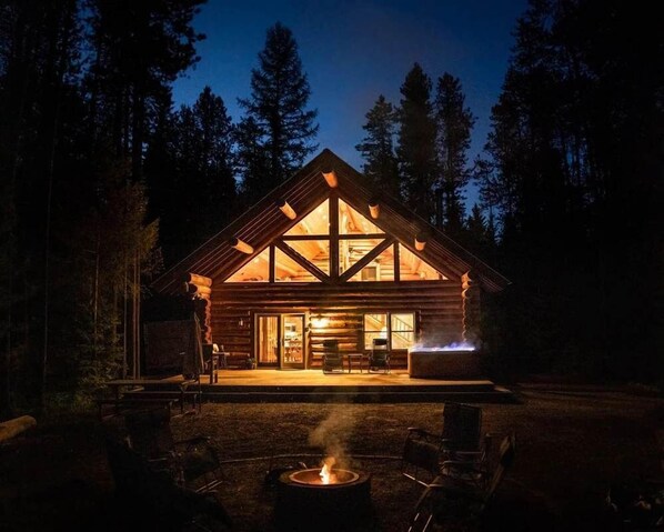 Una cabaña de troncos con un pozo de fuego y zona de estar al aire libre.