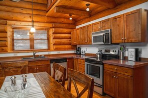 Una cocina tipo cabaña de madera con una mesa de comedor, sillas, estufa, horno, microondas y cafetera.