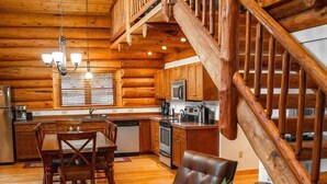 Ein Blockhaus-Interieur mit Essbereich, Küche und einer Holztreppe.