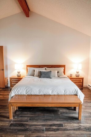 A bedroom with a wooden bed, two bedside tables with lamps, and a door. - Modern Lake House w/ Hot Tub and Dock (Whitefish)