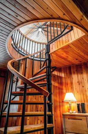 Escada espiral de madeira com um ventilador de teto, uma escrivaninha de madeira com abajur e uma parede de madeira.