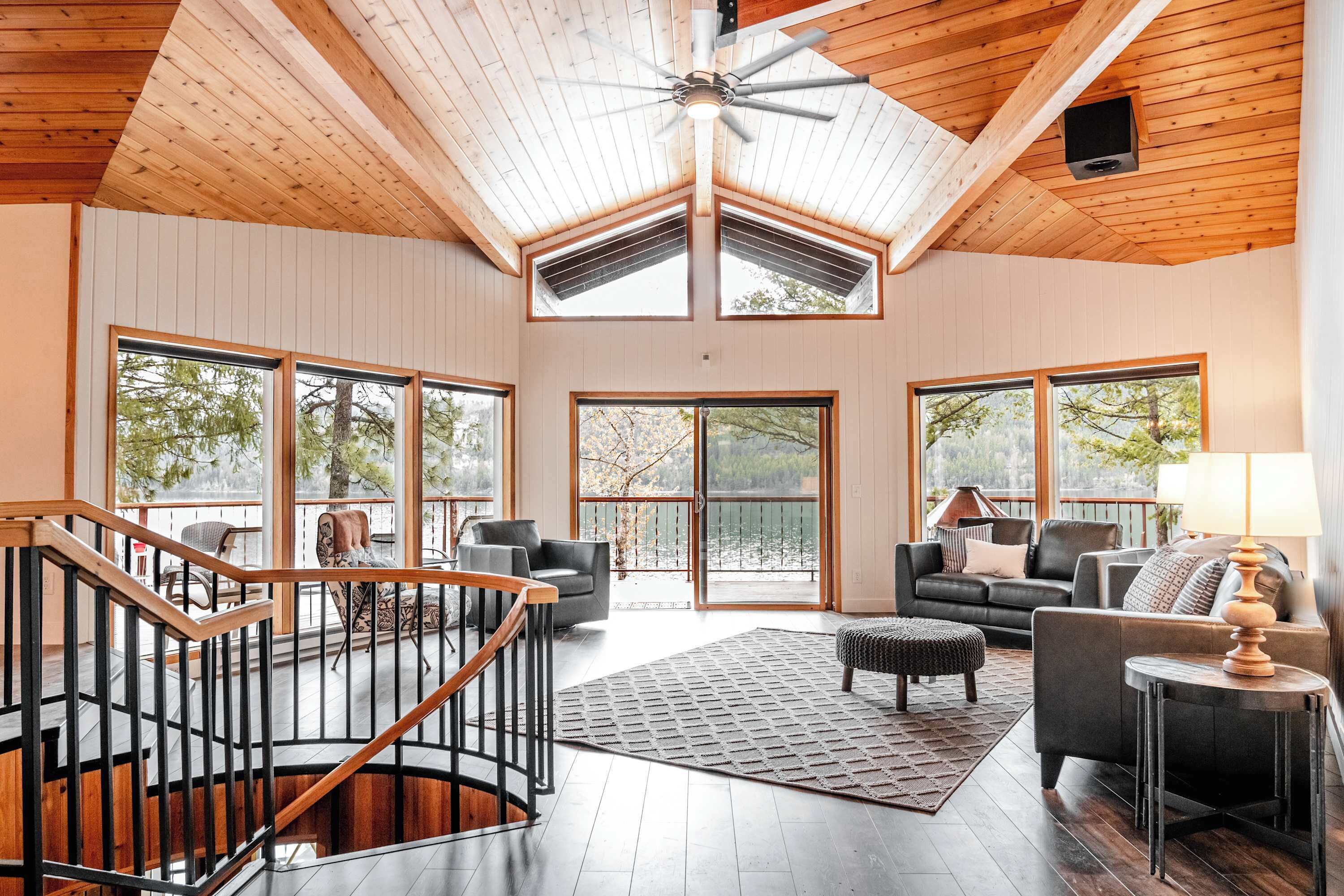A spacious living area with a high ceiling, large windows, and a wooden staircase.