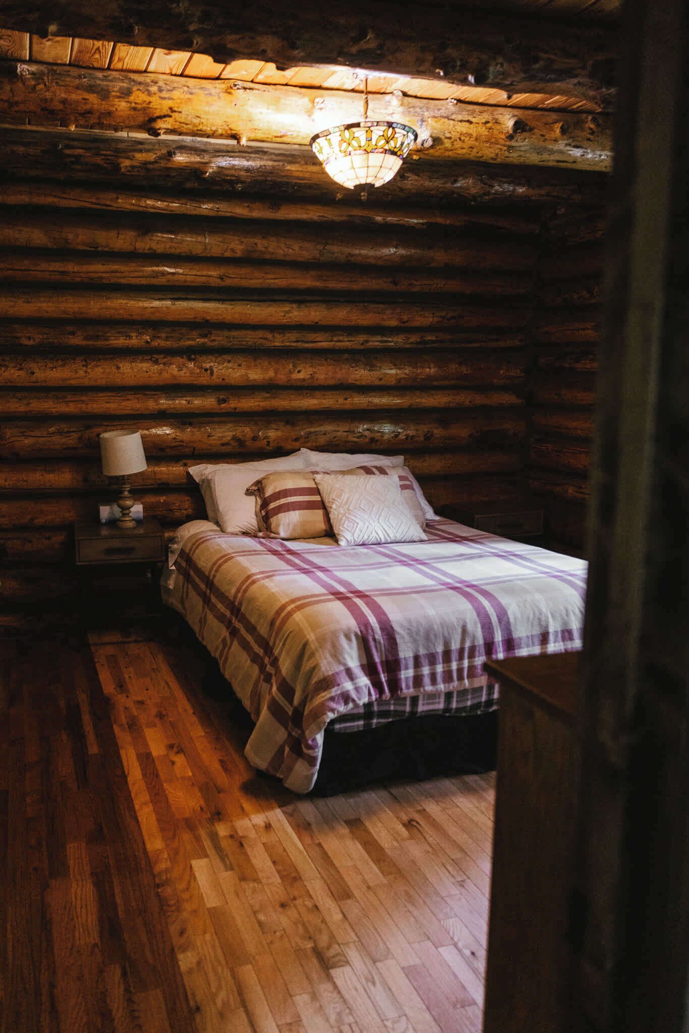 Ein Schlafzimmer in einer Blockhütte mit einem Bett, einem Nachttisch, einer Lampe und einer Pendelleuchte.