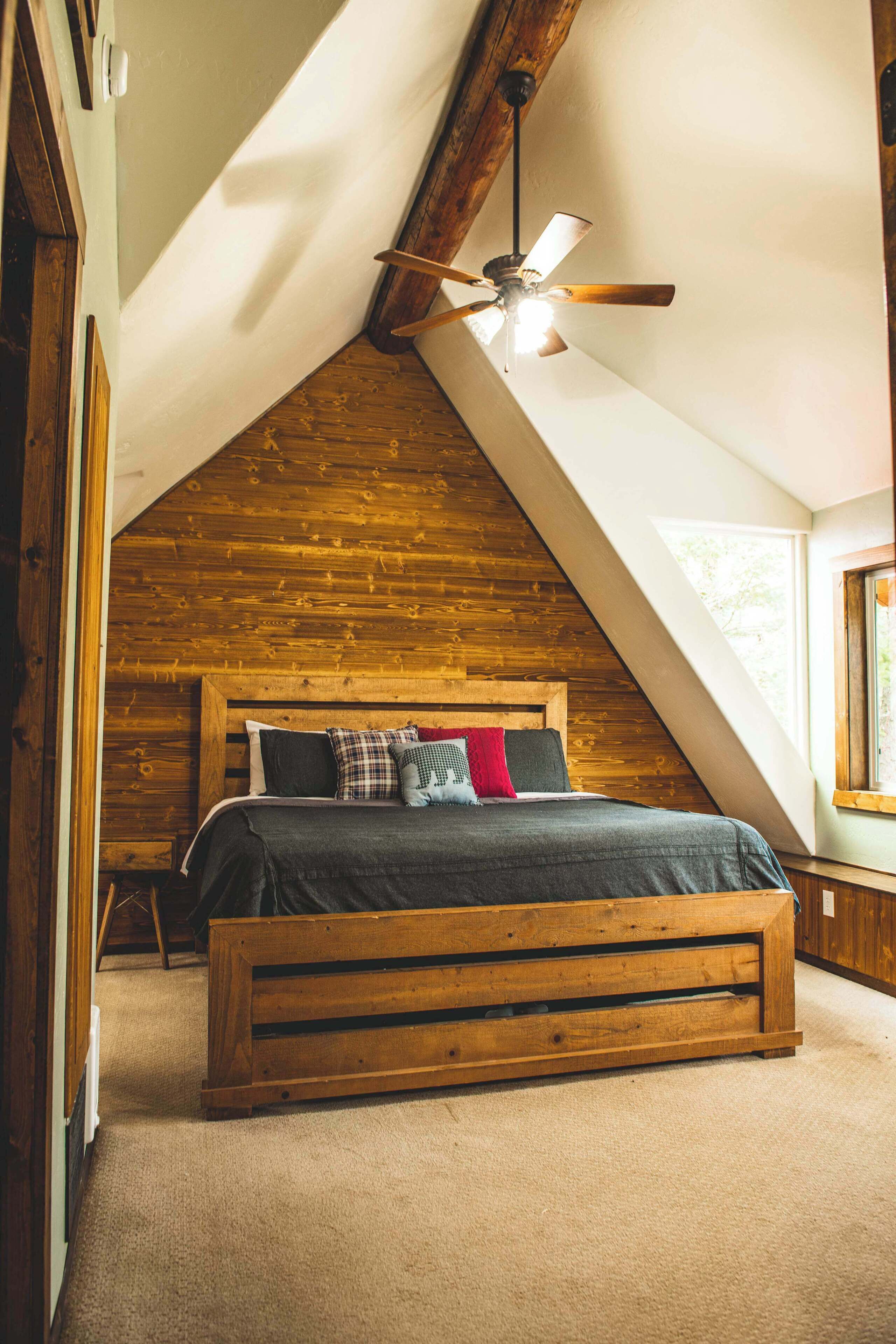 Ein Schlafzimmer mit geneigter Decke, einem hölzernen Bett und einem Deckenventilator.