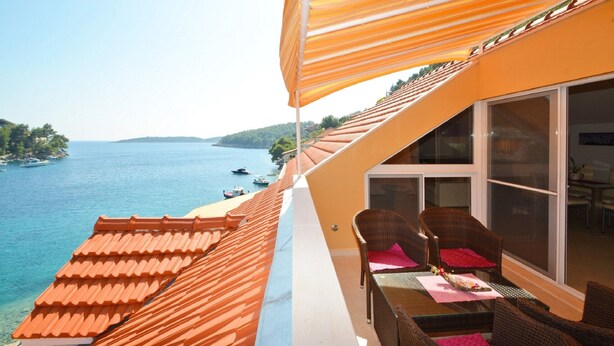 Un balcone con vista sul mare, mobili in vimini e un tenda a righe.