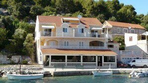 A multi-story building with balconies, a restaurant, and boats docked in the water. - Apartments Korčula - Two Bedroom Apartment with Terrace and Sea View (Prižba)