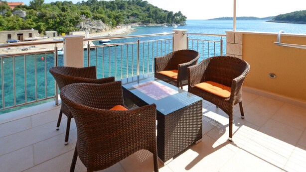 A balcony with wicker furniture and a glass table, overlooking a coastal area with boats and greenery. - Apartments Korčula - Two Bedroom Apartment with Terrace and Sea View (Prižba)