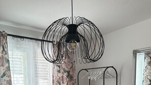Une pièce avec un lustre noir en fil de fer, des rideaux à motifs floraux, un présentoir métallique et un miroir.