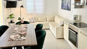 Une cuisine moderne avec un coin repas, comprenant une table en bois, des chaises vertes, un canapé et un four encastré.