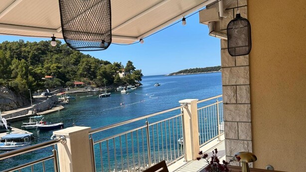 Un balcon avec vue sur la mer, les bateaux et une colline boisée.