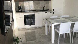 Ett modernt kök med vita skåp, en inbyggd ugn och en matplats med ett glasbord och vita stolar.
