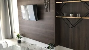 Ett modernt vardagsrum med en platt-TV som är monterad på en mörk trävägg, ett soffbord i glas och en minimalistisk hyllsektion med dekorativa föremål.