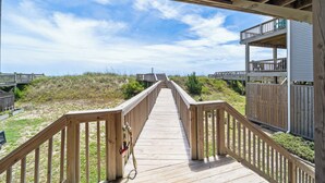 Une promenade en bois menant à une propriété située en bord de mer, dotée d’un balcon et offrant une vue sur l’océan.