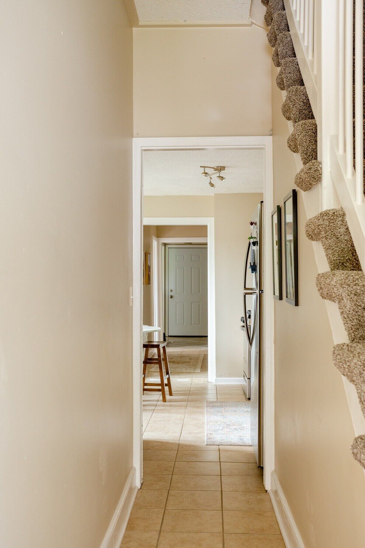 A hallway with a staircase on the right, leading to a dining area with a table and chairs.