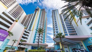 A modern hotel with multiple high-rise buildings, a central entrance, and palm trees.