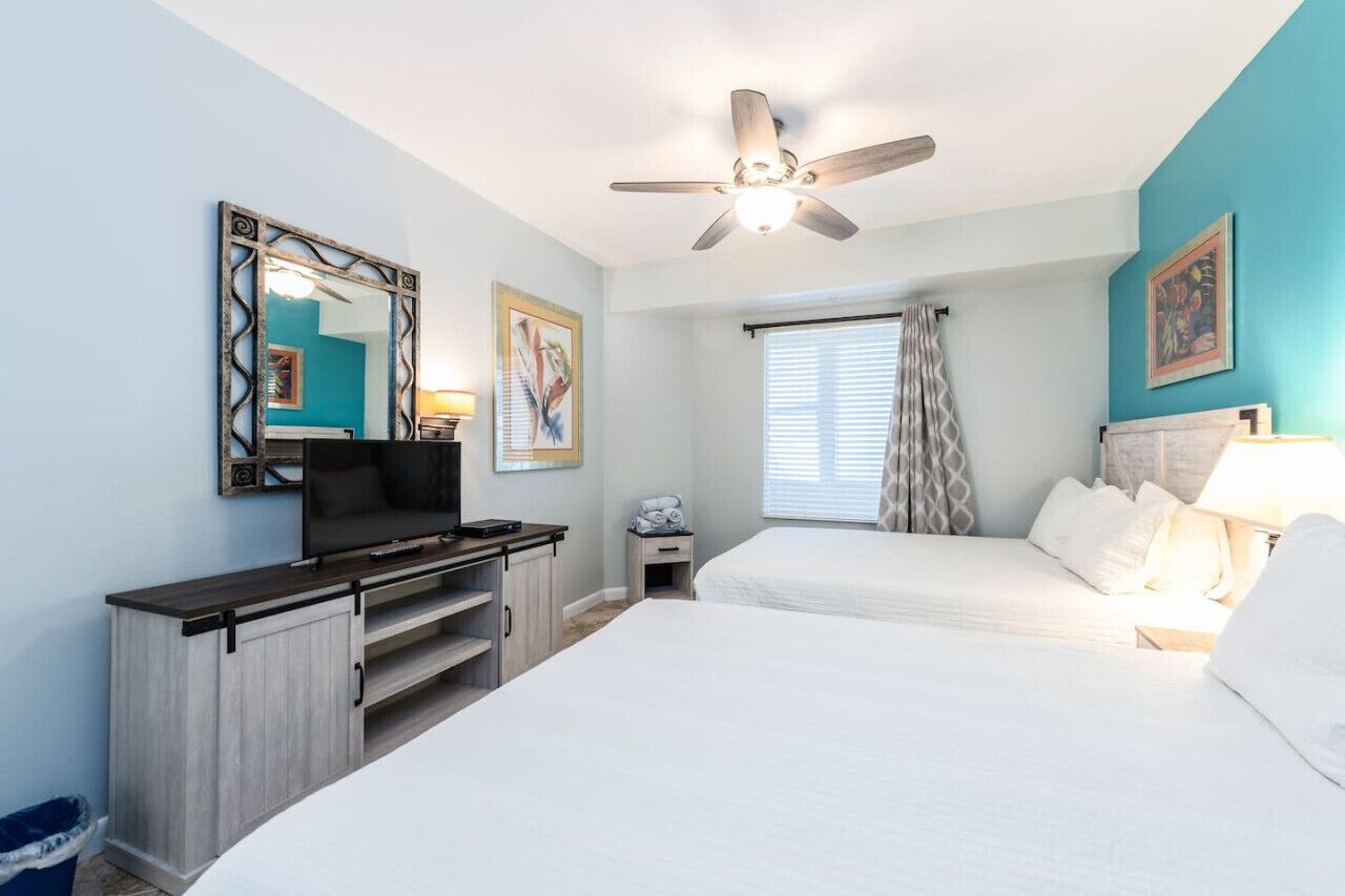 A bedroom with a bed, a TV, a ceiling fan, and a window with curtains.
