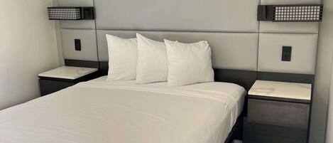 A modern hotel room with a large bed, two bedside tables, and a headboard with built-in lighting.