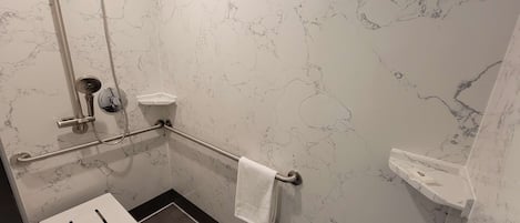 A modern bathroom with a marble wall, a shower with a handheld showerhead, a grab bar, a white sink, and a towel rack.