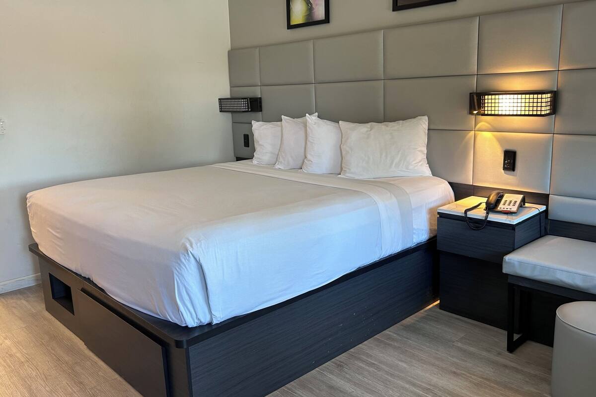 A modern hotel room with a large bed, a bedside table with a lamp, and a small seating area.
