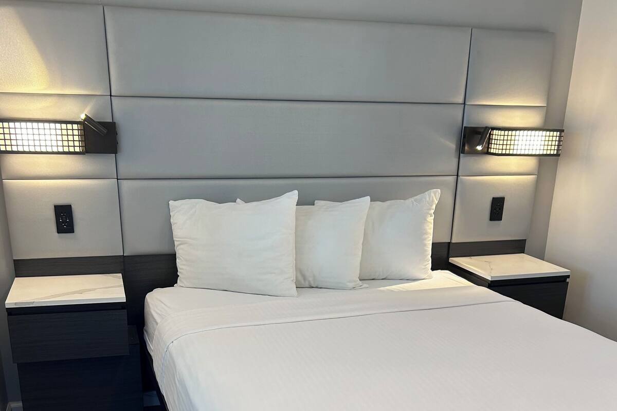 A modern bedroom with a large bed, two bedside tables, and wall-mounted lighting.