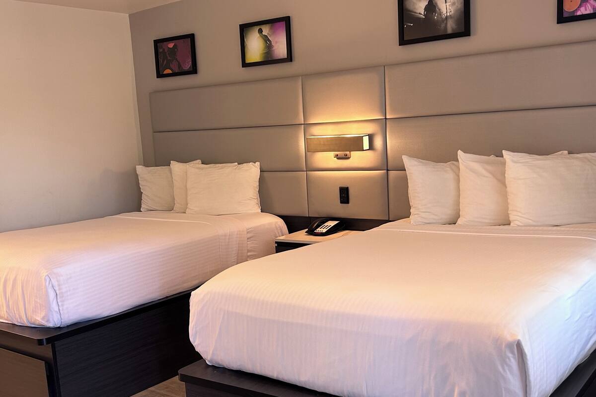 A hotel room with two single beds, a bedside table with a phone, and a wall-mounted light fixture.