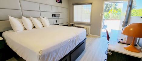 A modern bedroom with a large bed, a bedside table, a desk, and a window.