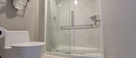 Un baño moderno con ducha envuelta en vidrio, inodoro y toallero.