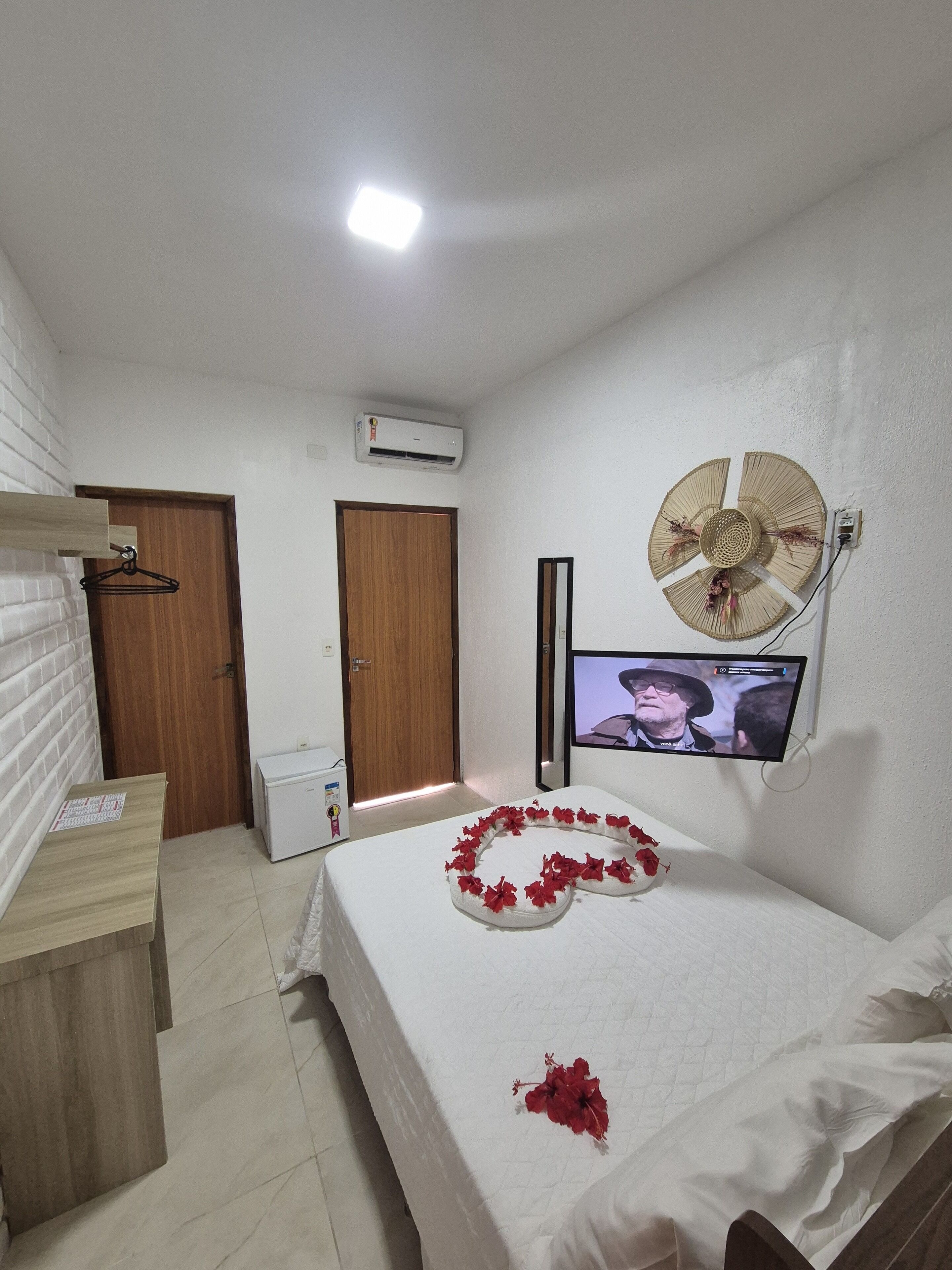 Una habitación de hotel con cama, televisión montada en la pared, equipo de aire acondicionado y puerta de madera.