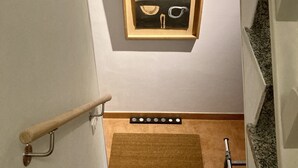 Un escalier avec une rampe, un tableau encadré accroché au mur, un paillasson et une échelle en métal.