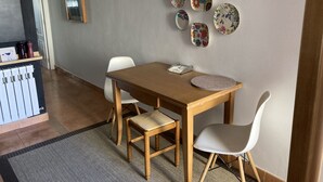 Un coin repas comprenant une table en bois, deux chaises, une petite table ronde et un luminaire fixé au mur.