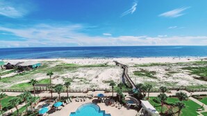 Un complex turístic a la platja amb zona de piscina, palmeres i vista a l'oceà.