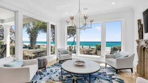 A spacious living room with a large window overlooking a beach, a round coffee table, and white sofas. - PoppyLu - Secluded Beachfront Home in Blue Mountain Beach with Private Pool & Golf Cart (Santa Rosa Beach)