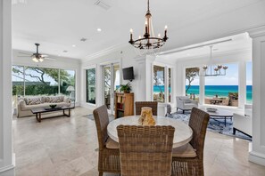 A spacious living area with a round table, wicker chairs, a ceiling fan, and large windows offering ocean views. - PoppyLu - Secluded Beachfront Home in Blue Mountain Beach with Private Pool & Golf Cart (Santa Rosa Beach)
