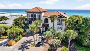 A two-story house with a beach view, surrounded by palm trees and a paved driveway. - PoppyLu - Secluded Beachfront Home in Blue Mountain Beach with Private Pool & Golf Cart (Santa Rosa Beach)