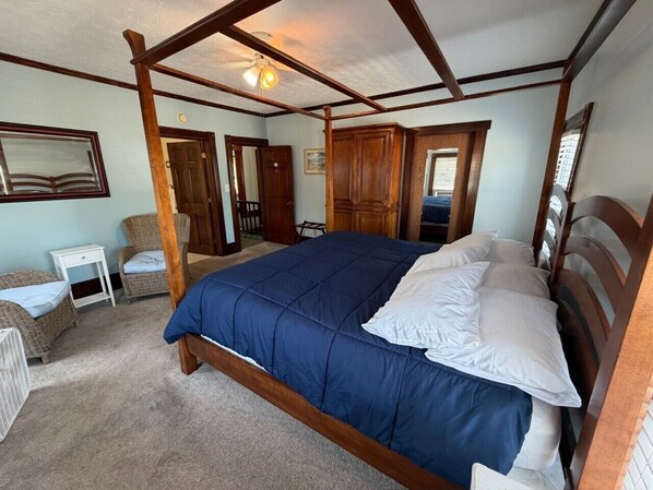 A bedroom with a four-poster bed, a small white nightstand, wicker chairs, and a ceiling fan.