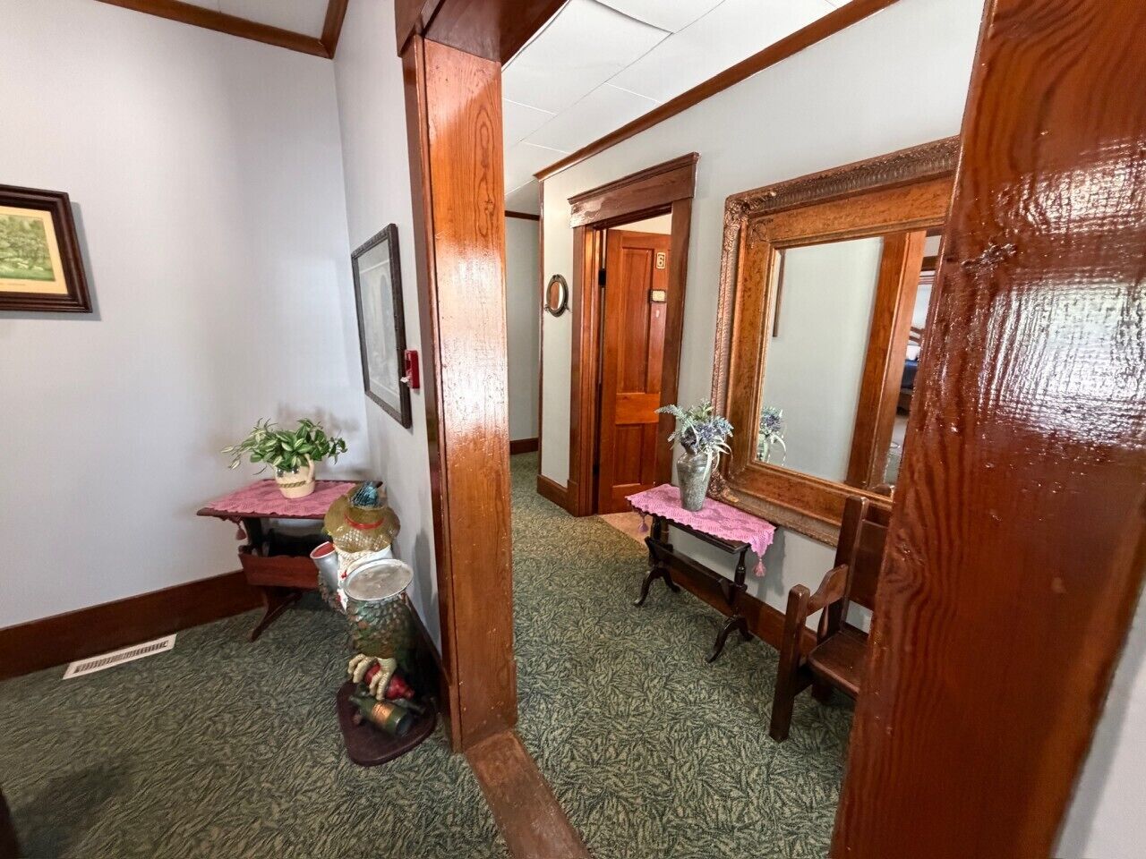 Un couloir avec une porte en bois, un miroir, une petite table sur laquelle se trouve un vase, et un banc.