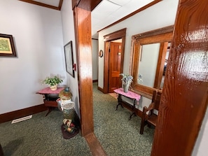 A hallway with a wooden door, a mirror, a small table with a vase, and a bench.