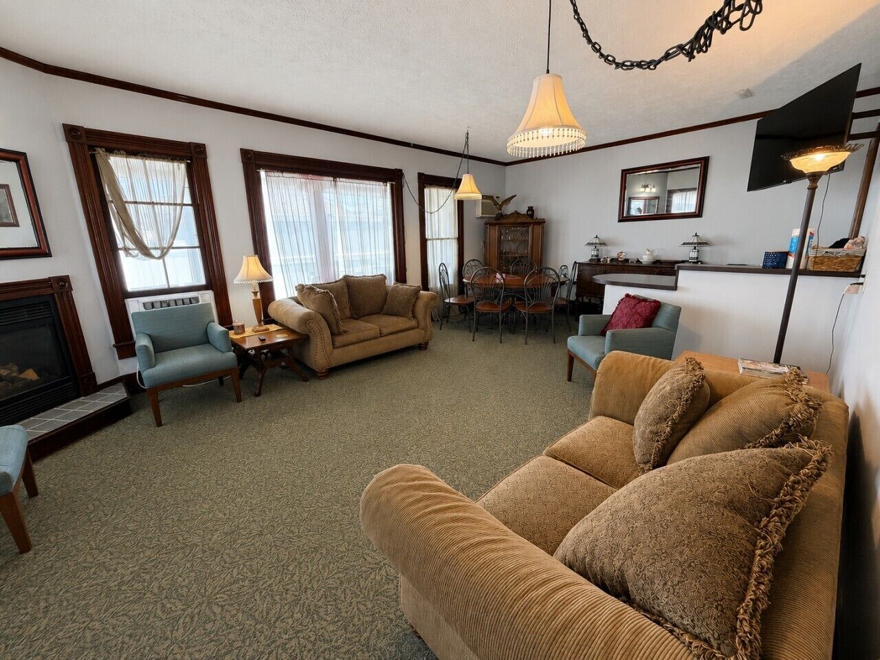 A living room with a fireplace, two sofas, a dining table with chairs, and a chandelier.