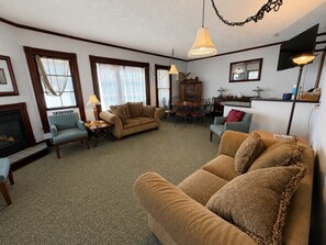 A living room with a fireplace, two sofas, a dining table with chairs, and a chandelier.